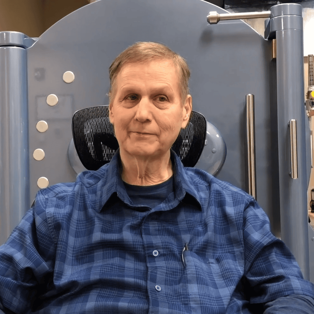 Older man sitting, wearing a blue shirt.