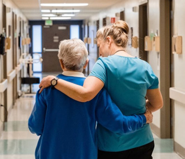 Caregiver supporting elderly person in hallway.