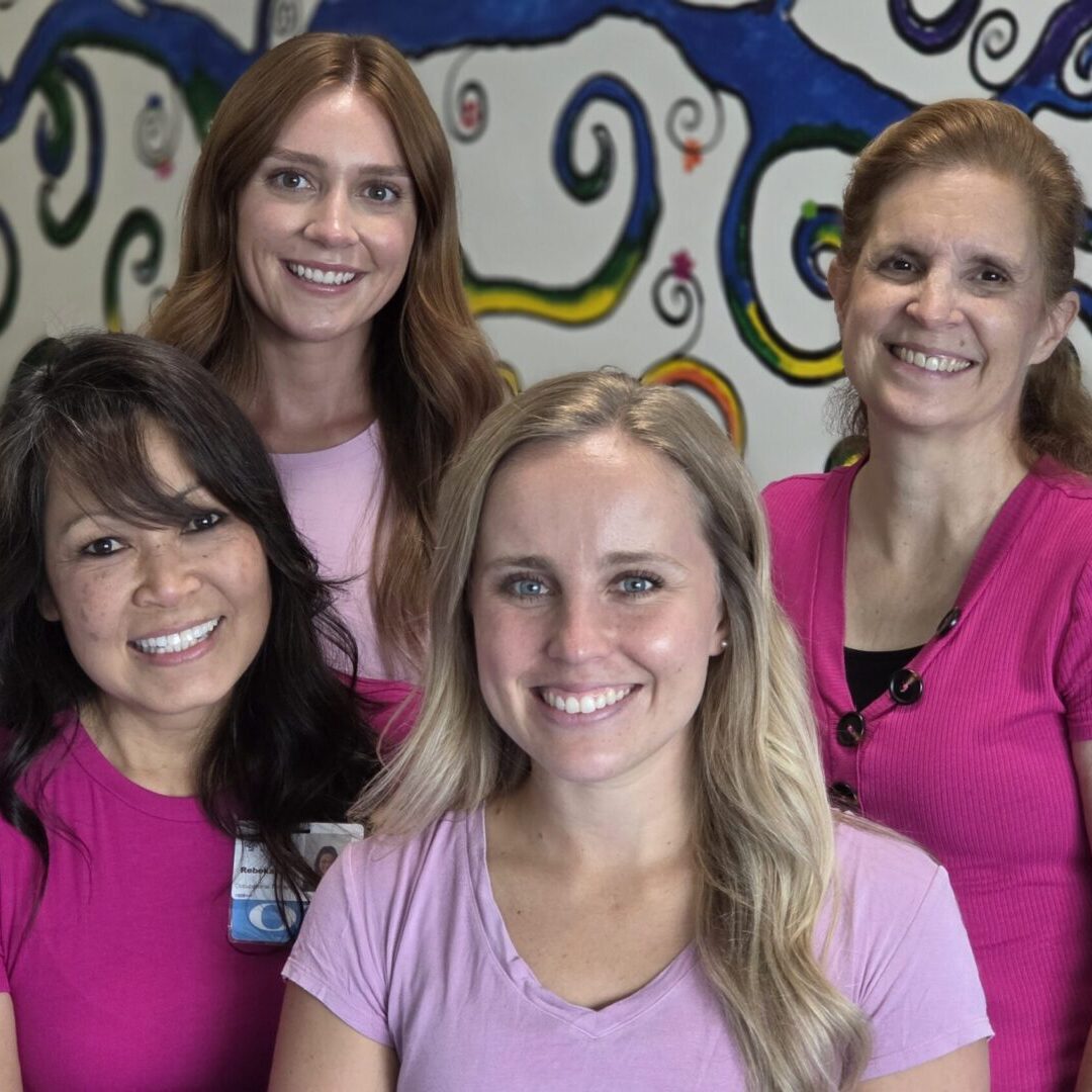 Four smiling women in pink shirts.
